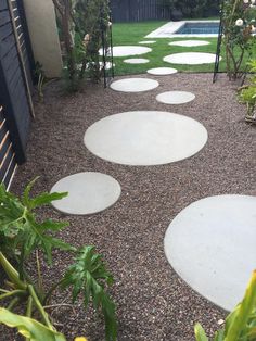 a garden with white stepping stones in the ground and green plants on either side of it