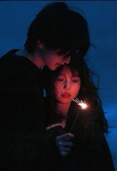 two people standing next to each other looking at a cell phone with sparklers in their hands