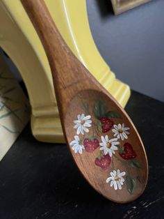 a wooden spoon with flowers and strawberries painted on the side sitting on a table