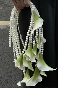 a woman is holding some white flowers and pearls on her long strand of necklaces