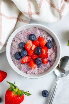 a bowl of oatmeal with strawberries and blueberries on the side