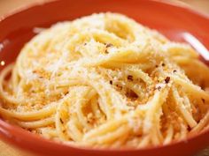 a red bowl filled with pasta and parmesan cheese on top of a wooden table