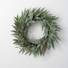 a wreath with green leaves and berries hanging on the wall next to a white wall