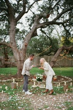 a man and woman standing next to each other in front of a tree with candles