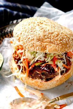 a hamburger with coleslaw, lettuce and carrots on the side