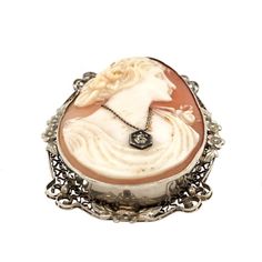 This is part of Chairish’s Fine Jewelry assortment.  A lovely Art Nouveau period 10K white gold pin/pendant featuring a carved shell cameo. The cameo has nice high relief and detailed carvings and depicts the profile of a lovely woman. Her hair is swept up with roses and she has one on the shoulder of her gown. She is wearing a diamond pendant. The frame of the cameo is white gold filigree with applied flowers. The piece is not marked, but tests 10K. There is a swivel bale to allow it to be worn Gold Pin, Carved Shell, High Relief, Pin Pendant, Gold Filigree, Diamond Pendant, Her Hair, Art Nouveau, Period