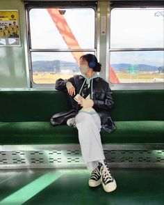 a woman sitting on a train seat with her headphones in her ears, looking out the window