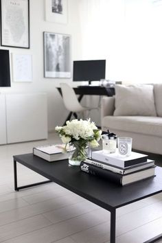 a coffee table with books and flowers on it in front of a white couch, framed pictures