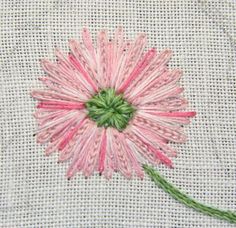 a pink flower with green stems on a piece of cloth that has been stitched together