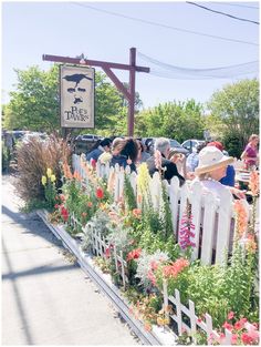 people are standing in front of a white picket fence with flowers and plants growing on it