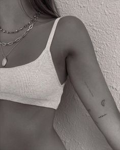 a woman with a tattoo on her arm wearing a white top and silver chain necklace