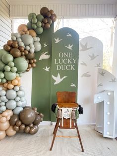 a chair sitting in front of a sign that says one lucky duck with balloons all around it