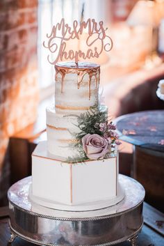 a three tiered wedding cake with frosting and flowers on the top is sitting on a table