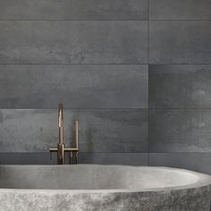 an oval bathtub sits in front of a gray wall