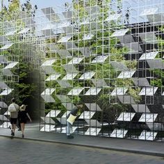 two people walking past an artisticly designed building with trees on the sides and windows