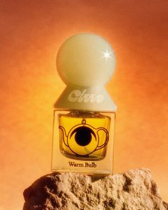 a bottle of perfume sitting on top of a rock next to an orange sky background