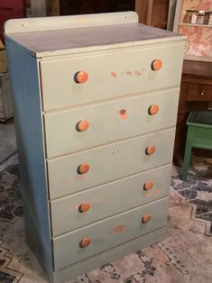 an old dresser with orange knobs on the top and bottom drawers, in a room