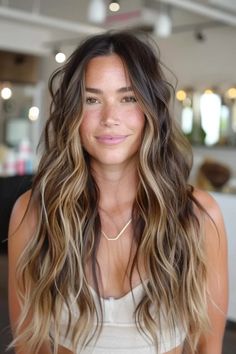 Woman with long wavy hair and blonde highlights smiling in a bright, modern salon. Dark Root Caramel Balayage, Natural Ombre Brunette, Brunette With Bright Highlights, Black To Honey Blonde Hair, Light Brown Hair With Front Highlights, Dark Brunette To Blonde Balayage Hair, Brunette Bronde Balayage Hair, Summer Burnett Balayage, Brown Long Hair With Highlights