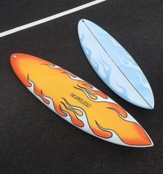 two surfboards with flames painted on them sitting in a parking lot next to each other