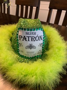 a bottle of silver patron sitting on top of a green furry chair cushion in front of a wooden table