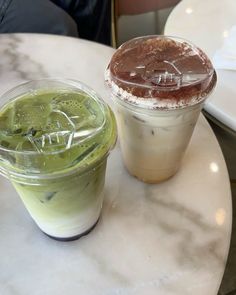 two drinks sitting on top of a white table next to each other in plastic cups