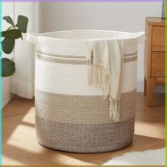 a white and brown basket sitting on top of a wooden floor next to a plant