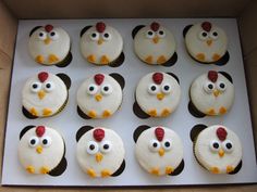 twelve cupcakes with white frosting decorated like chickens and rooster heads are in a box