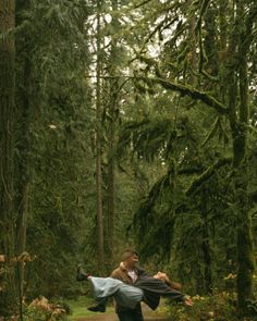 a man is walking through the woods carrying another man on his back with an umbrella