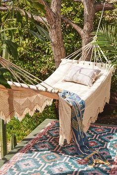 a hammock hanging from a tree in the middle of a yard with rugs and pillows