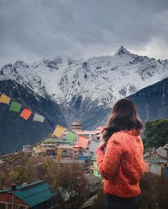 a woman standing on top of a mountain looking at the snow covered mountains