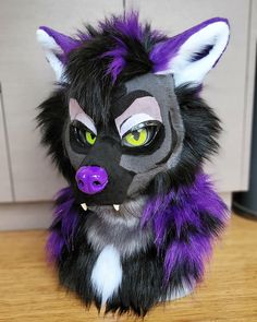 a stuffed animal with purple and black fur on it's head sitting on a table