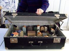 a woman standing next to a suitcase filled with miniature buildings