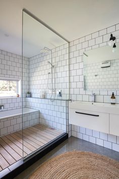 a bathroom with white tiles and wood flooring on the walls, along with a large glass shower door