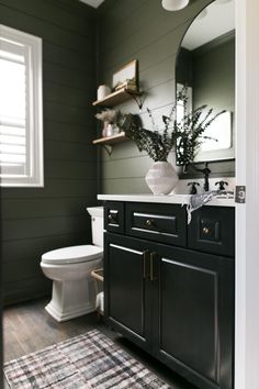 a white toilet sitting next to a bathroom sink under a mirror on top of a wooden floor