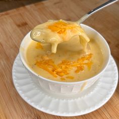 a spoonful of cheese soup is being held over the top of a white bowl