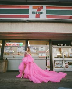 a woman in a pink dress is standing on the sidewalk near a 7 eleven store