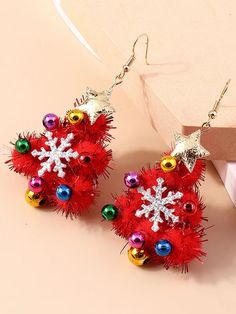 red and gold christmas decorations are hanging from the back of some earrings on a pink surface