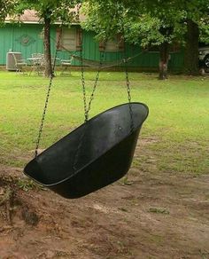 a black bathtub hanging from a tree in a yard next to a green house