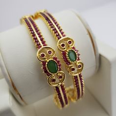 "* Handcrafted Gold Plated 2 Bangle Set. * Bangles are made with Semi-Precious Ruby and emeralds stones * High Quality 22 K Gold Plated- 2 Bangle set * 2.4 ( 2.30\" diameter of the inner circle) ; 2.6 ( 2.41\" diameter of the inner circle); * Sold as a set of 2. The gorgeous gold-plated bangle/ bracelet best exemplifies the careful craftsmanship done on it -- a specialty at Nemali Jewelry. It has a special tone of elegance attached to it. The intricate handmade design of the bangle/bracelet set Gold Emerald Bracelets For Wedding, Gold Emerald Bangle As A Gift, Traditional Gemstone Bangle For Anniversary, Ruby Gold Bangle For Celebration, Gold Bangle With Emerald As Gift, Gold Ruby Bangle For Celebration, Hand Set Ruby Round Bangle, Traditional Ruby Bangle Bracelets, Ruby And Emerald Bangles