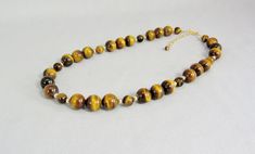 "This necklace showcases the contrasting bands of color and lustre in the large golden brown tiger eye beads in two sizes and separated with polished 14K gold filled accent beads. It is finished with a gold filled spring ring and attached 2.5\" gold filled adjustable chain. The necklace can be worn between 17.5 inches and 20 inches in length (44 to 51 cm). This is a timeless necklace that is easily worn with black, cream, white, brown, and gold blouses or sweaters--a very versatile piece! It shi Spiritual Brown Single Strand Jewelry, Brown Single Strand Round Jewelry, Brown Single Strand Round Bead Jewelry, Brown Jewelry With Polished Round Beads, Brown Single Strand Jewelry As A Gift, Brown Single Strand Jewelry For Gifts, Brown Single Strand Jewelry Gift, Brown Round Single Strand Jewelry, Gold Blouses