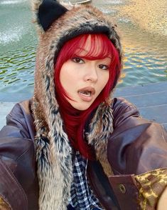 a woman with red hair wearing a furry hat and scarf over her head, posing for the camera