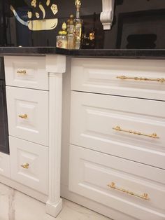 a white kitchen with black counter tops and gold pulls on the cabinets in front of it