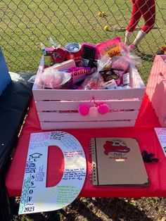 a red table topped with lots of items on top of a grass covered field next to a fence