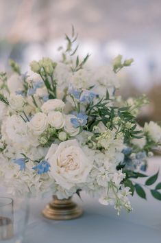 a vase filled with white and blue flowers on top of a table next to two glasses