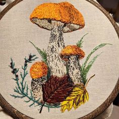 a close up of a embroidery on a piece of cloth with mushrooms in the background