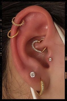 an ear with three different types of piercings on top of the ear and one is gold