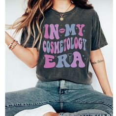 "🎨 Embrace your passion with our \"In my Cosmetology Era\" tee.  Whether you're a seasoned stylist or just starting your journey, this shirt is perfect for showing off your love for all things beauty.  🌈 Crafted from the best materials, this tee offers unrivaled comfort and durability, so you can slay in style all day long.  The relaxed fit ensures a comfortable and flattering look, while the vibrant colors add a pop of personality to your wardrobe.  💫 The \"In my Cosmetology Era\" design is Mom Era, Dance Mom, Groovy Retro, Retro Font, Gymnast, Fabric Softener, Look Plus, Mom Shirt, Teacher Shirts