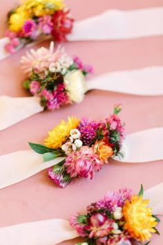 colorful bouquets of flowers are lined up on a pink tablecloth with white ribbons