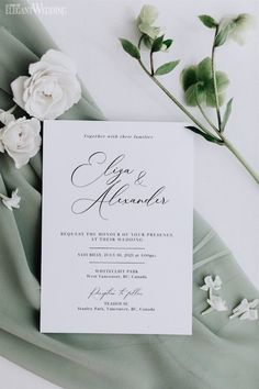 the wedding stationery is laid out on top of a green cloth with white flowers and greenery