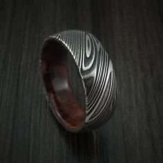 a silver ring with an intricate design on it sitting on a wooden surface in front of a black background